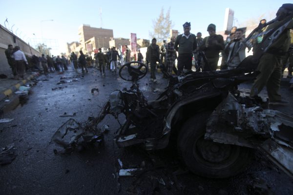 Policemen look at the wreckage of a car at the scene of a car bomb explosion outside the police college in Sanaa